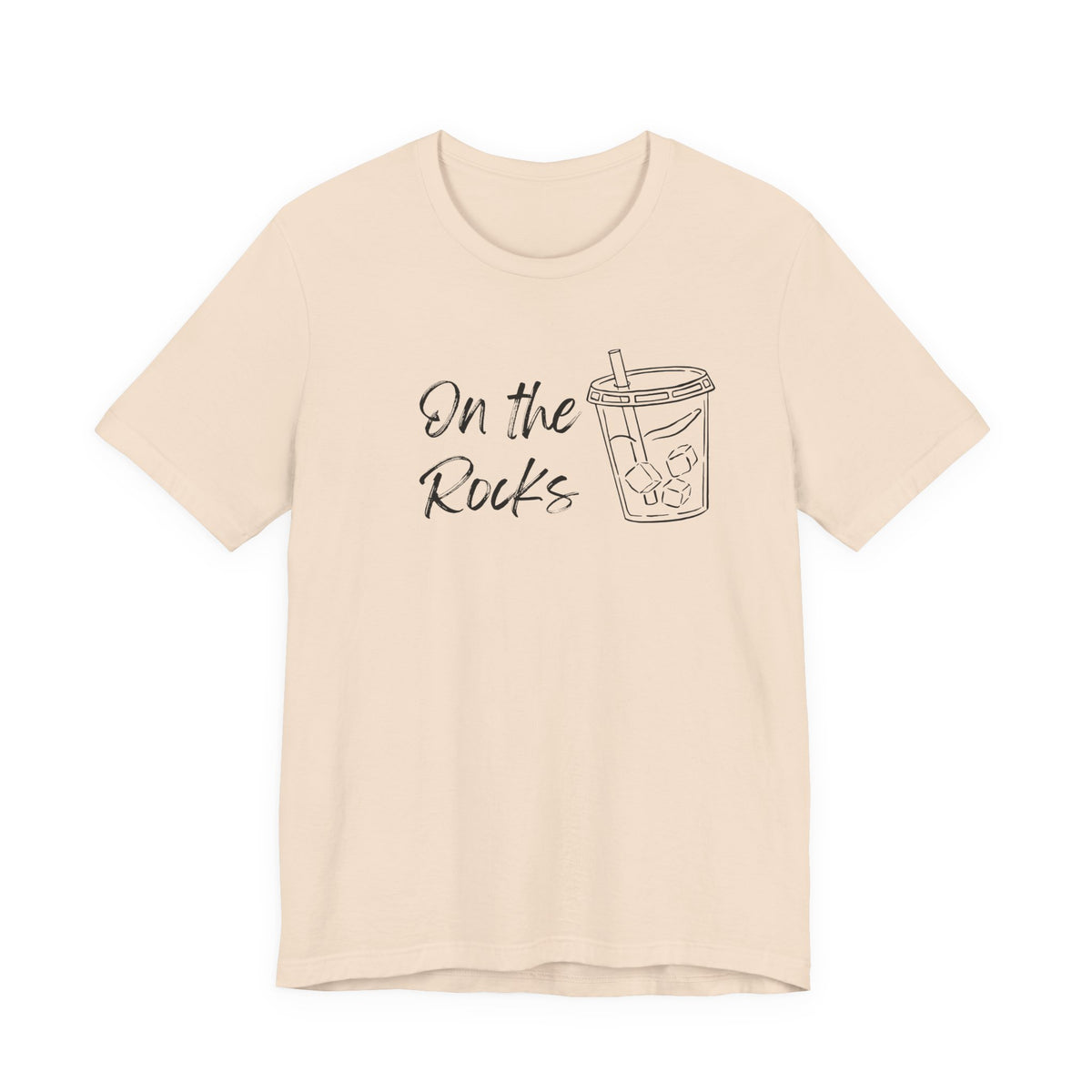 A light beige short-sleeve t-shirt with a black graphic print on the front that reads 'On the Rocks' next to a simple line drawing of a iced coffee cup, shown against a plain white background.