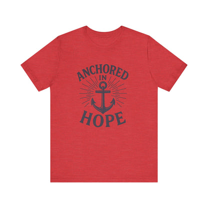 A heather red short-sleeve t-shirt with a dark navy graphic on the front featuring an anchor and the words 'ANCHORED IN HOPE'.