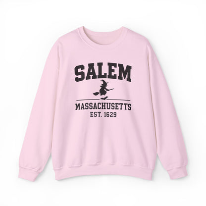 A light pink crewneck sweatshirt featuring a black graphic print on the front that reads 'SALEM MASSACHUSETTS EST. 1629' with a silhouette of a witch riding a broomstick.