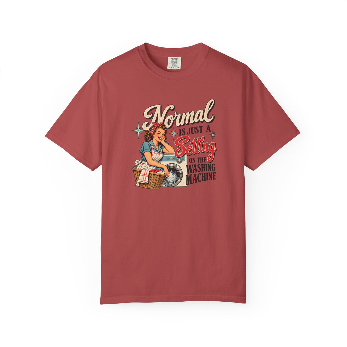 A short-sleeve crewneck t-shirt in a dusty rose or muted brick red color, featuring a vintage-style pin-up graphic of a woman washing clothes with the text 'Normal is just a Setting for the Washing Machine' printed on the front.