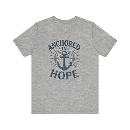A heather gray short-sleeve crewneck t-shirt featuring a navy blue graphic on the front with the words 'ANCHORED IN HOPE' surrounding an anchor and sunburst design.