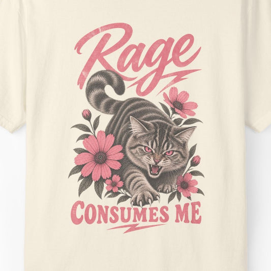 A close-up of a cream-colored t-shirt featuring a graphic print of a tabby cat surrounded by pink flowers and the text 'Rage CONSUMES ME' in pink lettering.