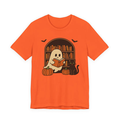An orange short-sleeve crewneck t-shirt featuring a Halloween graphic of a ghost reading a book in front of a bookshelf, with pumpkins, a black cat, and bats.