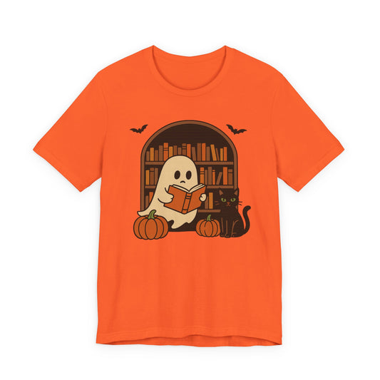 An orange short-sleeve crewneck t-shirt featuring a Halloween graphic of a ghost reading a book in front of a bookshelf, with pumpkins, a black cat, and bats.