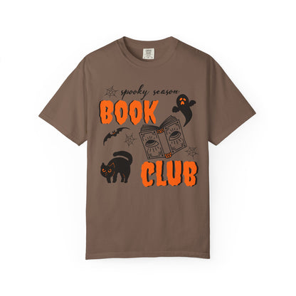 A brown short-sleeve crewneck t-shirt featuring a 'spooky season BOOK CLUB' graphic on the front with orange text, a black cat, a ghost, and a book illustration, displayed on a clean white background.