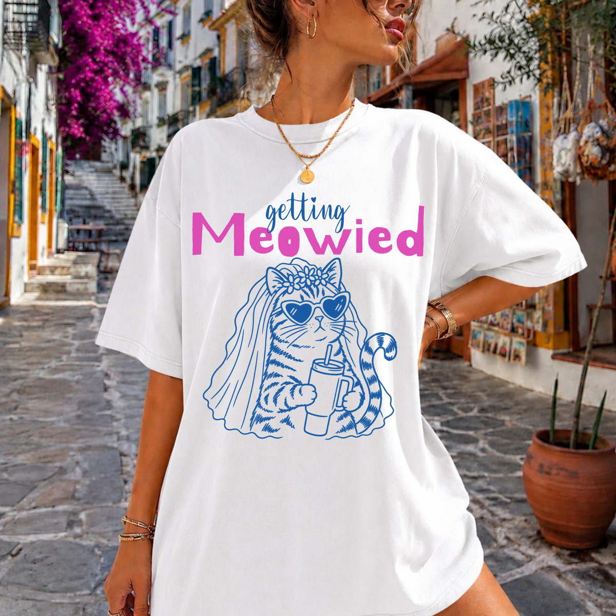 A woman wearing an oversized white graphic T-shirt with the text 'getting Meowied' and a blue cat illustration in a street setting.