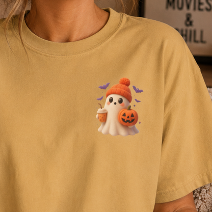 A person wearing a mustard yellow t-shirt with a cute cartoon ghost graphic on the chest. The ghost is white with a small orange beanie, holding a jack-o'-lantern and a drink, with small purple bats flying around it.