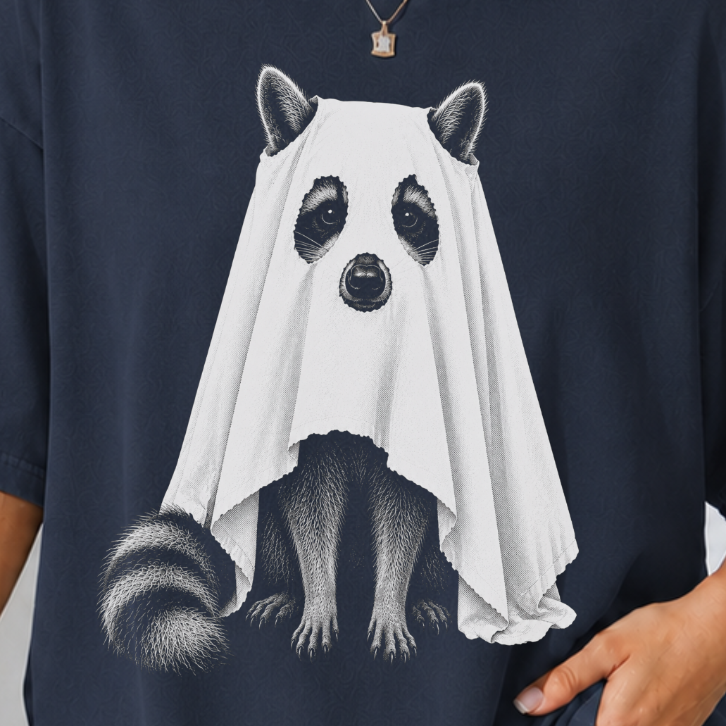 A woman wearing an oversized navy blue t-shirt with a graphic of a raccoon dressed in a white ghost, posed against a light gray wall.