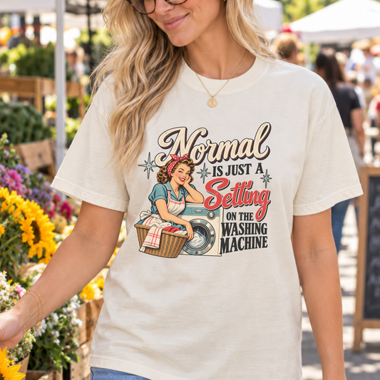 A woman wearing a cream-colored graphic t-shirt with a retro-style illustration and the text 'Normal is just a Setting on the Washing Machine' at an outdoor flower market.