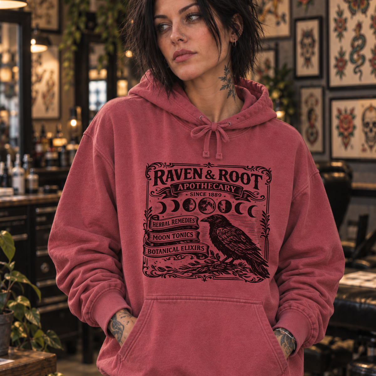 woman in tattoo shop wearing Raven & Root apothecary Sweatshirt from Comfort Colors in Crimson color.
