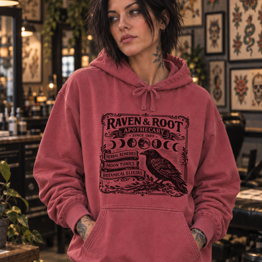 woman in tattoo shop wearing Raven & Root apothecary Sweatshirt from Comfort Colors in Crimson color.
