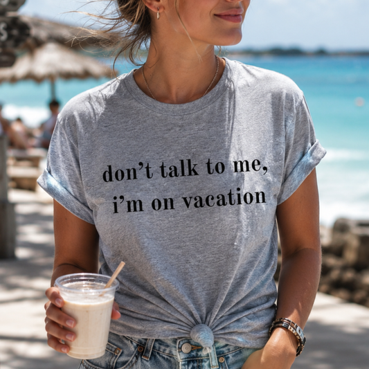 Person wearing a gray t-shirt with 'don't talk to me, I'm on vacation' text at a beach.