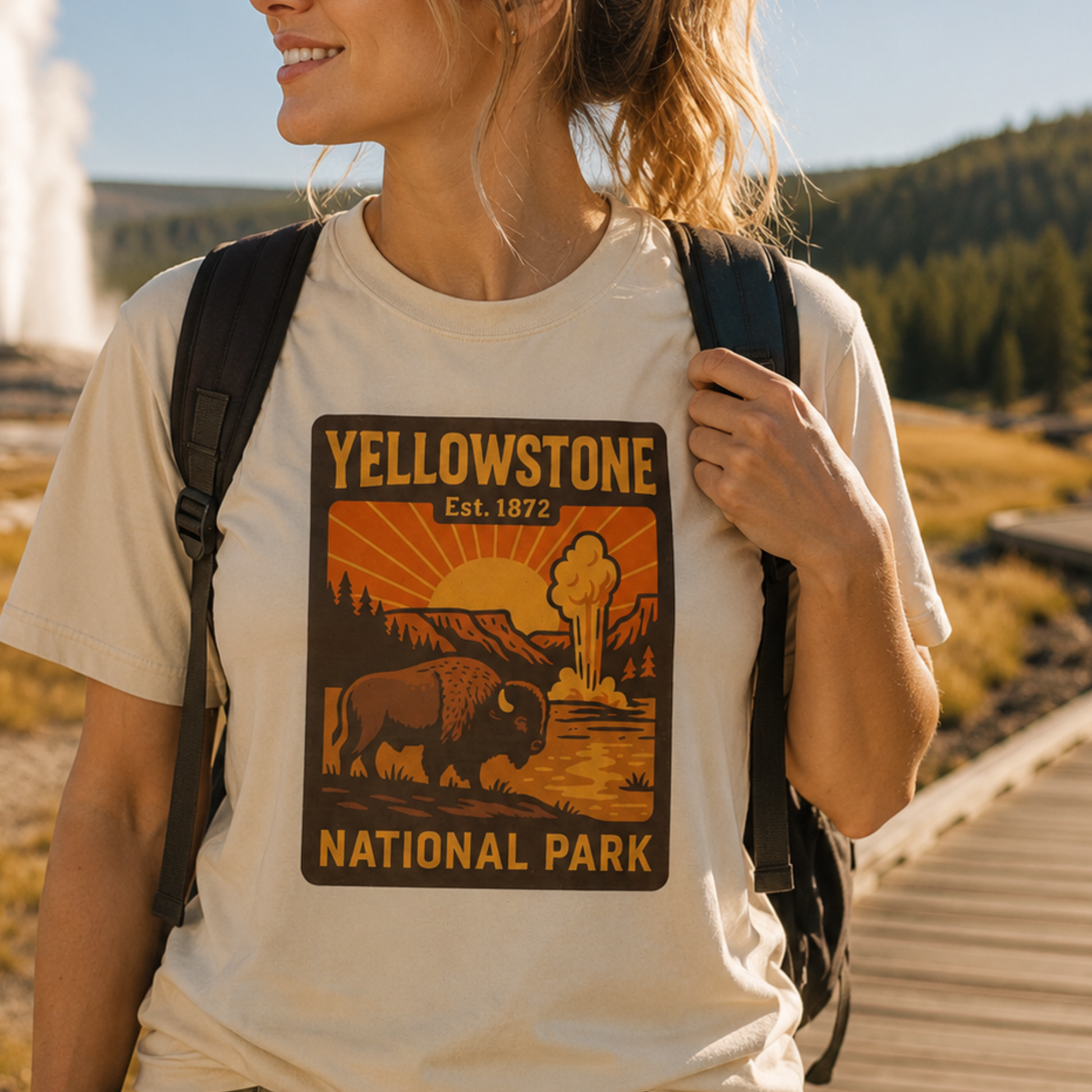A woman wearing a cream-colored t-shirt with a Yellowstone National Park graphic print, carrying a black backpack in an outdoor park setting.
