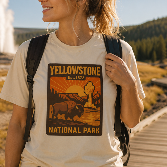 A woman wearing a cream-colored t-shirt with a Yellowstone National Park graphic print, carrying a black backpack in an outdoor park setting.